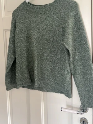 Grön stickad tröja från Vero Moda - Mysig grönmelerad stickad tröja från Vero Moda med rund halsringning och ribbade muddar vid ärmslut och nederkant. Perfekt för lager-på-lager och enkel att matcha med jeans eller kjol. Använd några fåtal gånger och är i perfekt skick! 