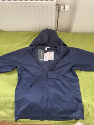 Blå vindjacka Woolrich - Snygg blå vindjacka från Woolrich med huva och dragkedja framtill. Jackan har två snedställda fickor med dragkedja och diskret logga på bröstet. Tillverkad i lätt och slitstarkt material, perfekt för blåsiga dagar. Justerbar vid midjan🤩
