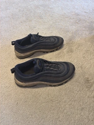 Nike Air Max 97 blå sneakers - Nike Air Max 97 sneakers i blå med vågformade detaljer och synlig Air-sula. Skorna har snörning och en diskret blå Nike-logga på plösen. Ovandelen är i syntet och textil för en sportig look.