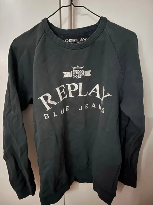 Grön sweatshirt från Replay - Cool svart sweatshirt från Replay med stort vitt tryck på bröstet där det står 'Replay Blue Jeans' och en liten logga ovanför. Tröjan har rund halsringning och långa ärmar. Perfekt för en avslappnad och stilren look.                         Längd: 65 cm                                                       Bröstvidd: 53 cm