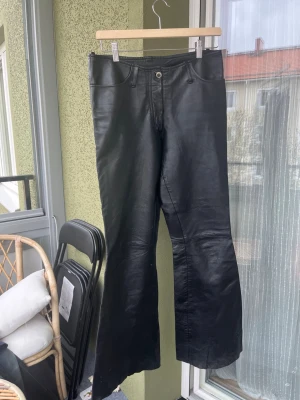 Svarta skinnbyxor bootcut Roccobaroco - Svarta skinnbyxor från Roccobaroco i bootcut-modell. Byxorna har hög midja, klassisk femficksdesign och dragkedja framtill. Snyggt glansigt skinnmaterial som ger en cool vibe.