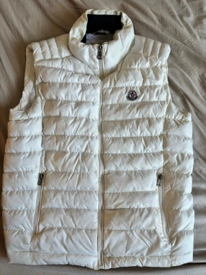 Vit dunväst från Moncler - Snygg vit dunväst från Moncler. Säljer pågrund av att den aldrig används, så iprincip i nyskick. Passar strl herr M/L. Kvitto finns ej men äkthet kan varifieras via qr kod samt detaljer i målningen