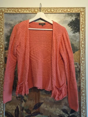 Rosa stickad kofta med fransar - Säljer en rosa stickad kofta från Zara Knit med snyggt strukturmönster och långa ärmar. Koftan har öppet fall och coola fransdetaljer vid fickorna. Perfekt för lager-på-lager och ger en chill vibe till din outfit. 100% bomull