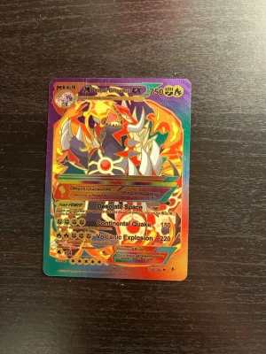 Pokémonkort Mega Primal Groudon EX - Säljer ett färgstarkt och holografiskt Pokémonkort med motivet Mega Primal Groudon EX. Kortet har en mix av orange, röd, gul och lila färg med coola effekter och detaljer. Perfekt för samlare eller Pokémon-fans som vill utöka sin samling.