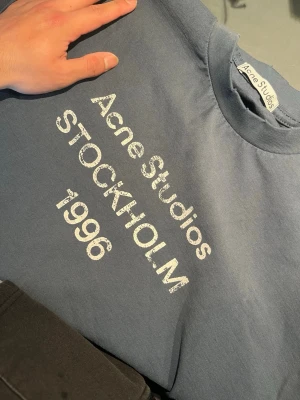 Marinblå Acne Studios long sleeve - Säljer en marinblå från Acne Studios med vit text 'Acne Studios STOCKHOLM 1996' på framsidan. Klassisk rund halsringning och avslappnad passform. Perfekt för dig som gillar stilrena och trendiga plagg med tydlig logga.