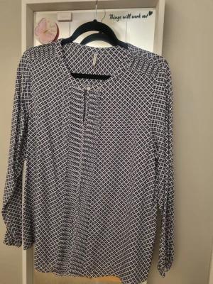 Mönstrad blus i blått och vitt - Snygg blus med småblommigt mönster i blått och vitt. Blusen har rund halsringning, knappdetalj framtill och långa ärmar. Tillverkad i ett lätt och luftigt tyg som ger en avslappnad känsla. 