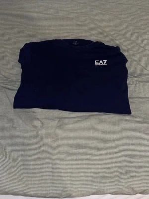 Mörkblå långärmad tröja EA7 - Snygg mörkblå långärmad tröja från EA7 Emporio Armani med rund halsringning och vit logga på bröstet. Enkel och stilren design som passar perfekt till jeans eller joggers. Mjukt material för en bekväm känsla.