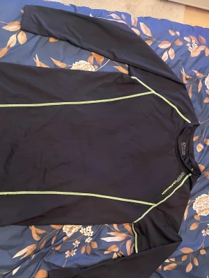 Svart kompressionströja OTP L - Svart långärmad kompressionströja från OTP med neongröna sömmar. Tillverkad i ett stretchigt och fukttransporterande material som passar perfekt till träning och sportaktiviteter. Snygg passform och diskret logga vid halsen.