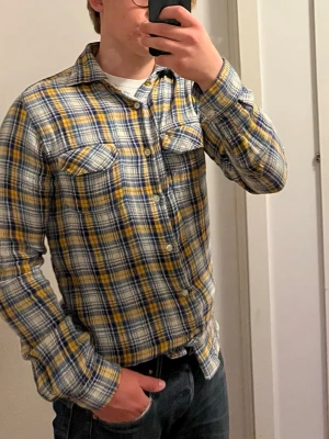 Riktig skön Nudie skjorta  - Säljer en shyyst rutig nudie skjorta i blått, gult och vitt 👔.Skön flanell som ger en fin sommarkänsla☀️. Perfekt för dig som gillar en avslappnad men ändå snygg stil. Hör gärna av dig vid frågor❓