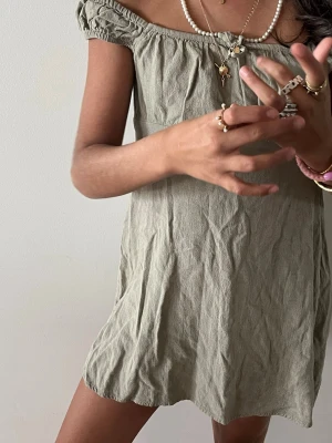 Ljusgrön kort offshoulder klänning - Söt kort klänning i ljusgrönt linne med offshoulder-modell och lätt rynkade detaljer upptill. Klänningen har en avslappnad passform och är perfekt för varma dagar. Enkel och stilren design som är lätt att matcha med accessoarer.