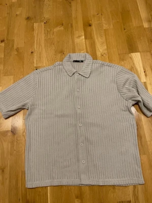 Lager 157 Beige ribbad skjorta med kort ärm - Säljer en beige skjorta från Lager 157 med ribbad struktur och korta ärmar. Skjortan har klassisk krage och knäppning framtill. Perfekt för dig som gillar en clean och stilren look.