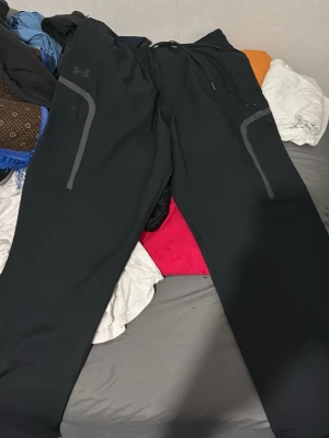 Svarta sportswear cargo pants från Under Armour - Byxorna är nya och jag säljer de för att de är för stora och det går inte att lämna tillbaka kläder i under armour. Jag säljer Svarta mjukisbyxor från Under Armour med gråa detaljer längs benen och logga på vänster sida. Byxorna har elastisk midja med snörning och är gjorda i ett mjukt och funktionellt material, perfekta för chill eller träning.