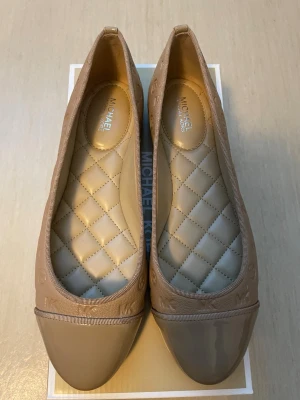 *NY*Arielle Ballet ballerinaskor Michael Kors stl 37 (7) - Nya i kartong i stl 7 (37). I färgen Camel. Med silverdetaljer (logo).  Normala i stl. Innermått 23,0 cm.   Ord pris: 1700 sek, Outlet: 1130 sek,  Pris nu:  500 sek