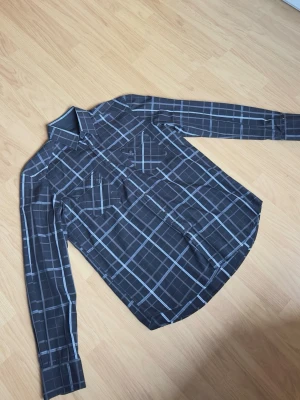 Jack & Jones svart/rutig skjorta – strl S - Stilren svart skjorta med grå/vita rutor från Jack & Jones. Skjortan har dubbla bröstfickor och passar perfekt både till vardag och mer uppklädda outfits.  Storlek: S, men sitter mer som en M i passformen. Skick: Bra skick utan större anmärkningar.  Modellen på bilden är ca 185 cm lång och väger ca 78 kg för referens.  Hör gärna av dig vid frågor eller intresse!
