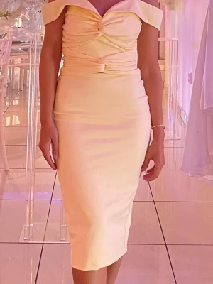 Ljusgul offshoulder klänning - Elegant ljusgul klänning med offshoulder-design och v-ringad urringning. Klänningen har figurnära passform, draperade detaljer framtill och är tillverkad i ett mjukt, stretchigt material. Perfekt för sommarens tillställningar.