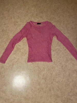Rosa stickad tröja med spetsmönster - Säljer en söt rosa stickad tröja med genombrutet spetsmönster. Tröjan har rund halsringning och långa ärmar. Perfekt för dig som gillar en feminin och trendig stil.