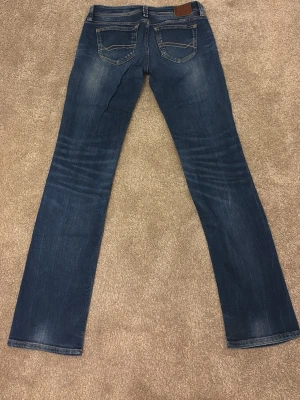 Blå Tommy Hilfiger Suzy Slim jeans - Snygga blå jeans från Tommy Hilfiger i modellen Suzy Slim. Jeansen har klassisk femficksdesign, smal passform och coola slitningar. Tillverkade i denim med detaljerade sömmar och Hilfiger-logga på bakfickan. Perfekta för en avslappnad och trendig look!❤️