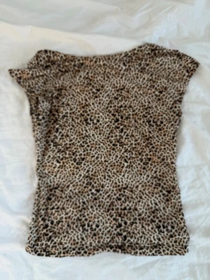 Leopardmönstrad topp i beige och svart - Säljer en snygg leopardmönstrad topp i beige och svart. Toppen har korta ärmar och är figurnära med mjukt, stretchigt material. Perfekt för dig som vill sticka ut lite extra med ett djurmönster.