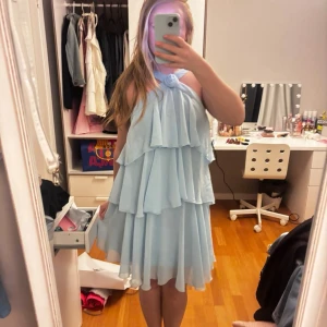 Ljusblå volangklänning - Superfin ljusblå kortklänning med flera lager volanger och en halterneck-design. Öppen rygg. Använd endast 1 gång, så i superfint skick!! Storlek S.