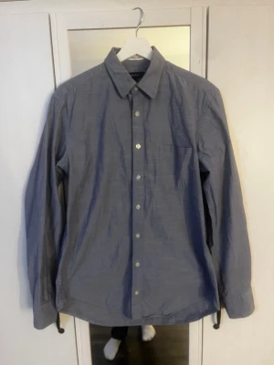 Blå skjorta från Gant - Klassisk blå skjorta från Gant med lång ärm, bröstficka och knappar framtill. Skjortan har en enkel, stilren design och är tillverkad i bomull för en bekväm känsla. Perfekt för dig som gillar en clean och avslappnad look. Hör av er vid frågor!