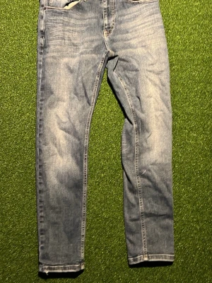 Ljusblå raka jeans - Säljer ett par ljusblå jeans med rak passform och klassisk femficksdesign. Jeansen har snygga slitningar och tvättade detaljer för en avslappnad look. Perfekta till sneakers och hoodie för en chill stil.