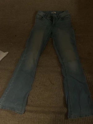 Blå bootcut jeans med fjärilsbrodyr - Säljer ett par blå bootcut jeans med snygg tvätt och broderade fjärilar på bakfickorna. Jeansen har klassisk femficksmodell och normal midja. Perfekta för dig som vill ha en unik detalj på dina jeans!