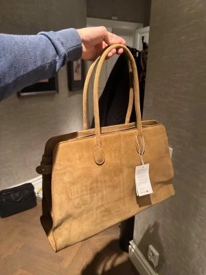 NA-KD Väska Mocka - Säljer en NA-KD väska i äkta mocka från deras premium kollektion, taggarna är fortfarande kvar.   Helt ny aldrig använd  Butikspris: 2000kr  Nu: 900kr   Modell: Big Suede Tote Bag  Färg: sand  https://www.na-kd.com/sv/produkter/big-suede-tote-bag-sand-1100-012080-0301