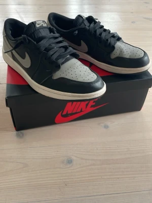  Air Jordan 1 Low og shadow - Snygga Nike Air Jordan 1 Low og shadow i svart och grått läder med klassisk Air Jordan-logga på hälen och Nike Swoosh på sidan. Skorna har gått upp lite inuti som syns på bilden men som inte känns när man har på sig de, kommer med ett häll skydd som man kan sätta på. Svart snörning, kommer även med vita. Perfekta för dig som gillar streetwear och ikoniska modeller. Ny pris i Sverige cirka 2300kr