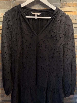 Svart kort klänning med broderi från  H&M - Hej!☀️Säljer en kort svart klänning från H&M med v-ringning och långa ärmar. Klänningen har broderade detaljer och hålmönster som ger en cool och trendig look. Volang nedtill för extra flow och feminin känsla. Perfekt för dig som gillar stilrena men ändå unika plagg. Funkar även som strandklänning💕