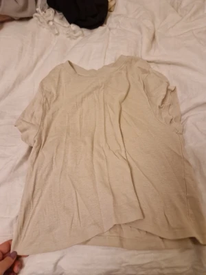 Beige basic t-shirt från H&M Divided - En enkel och stilren beige t-shirt från H&M Divided. T-shirten har rund halsringning och korta ärmar. Tillverkad i mjuk bomull som känns skön mot huden. Perfekt till jeans eller shorts för en avslappnad look.