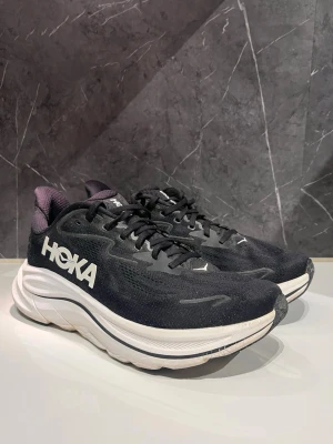 Hoka Clifton 10 - Snygga svarta löparskor från Hoka med stor vit logga på sidan och tjock, hög och vit mellansula. - Skorna är inte särskilt använda, säljer pga ej bra passform efter ett tag.                                                    - Snabb leverans, skickas samma dag.                             