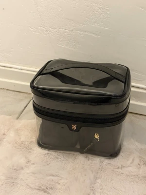 Transparent necessärset från Victoria's Secret - Säljer ett snyggt necessärset från Victoria's Secret med en transparent, svart väska och tre mindre svarta väskor. Perfekt för att organisera smink eller småprylar. Väskorna har guldfärgade dragkedjor och stilren design.