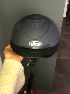 Mörkblå hjälm från Jacson - Snygg mörkblå hjälm från Jacson med matt finish och ventiler upptill. Justerbart hakband med snabbspänne och diskret logga framtill. Perfekt för dig som vill ha en stilren och funktionell hjälm till ridning eller annan aktivitet.