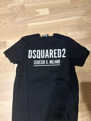 Svart DSQUARED2 t-shirt med tryck - Snygg svart t-shirt från DSQUARED2 med stort vitt tryck på bröstet där det står 'DSQUARED2 CERESIO 9, MILANO'. Klassisk rund hals och korta ärmar. Perfekt för dig som gillar streetwear och vill ha en statement-tee.