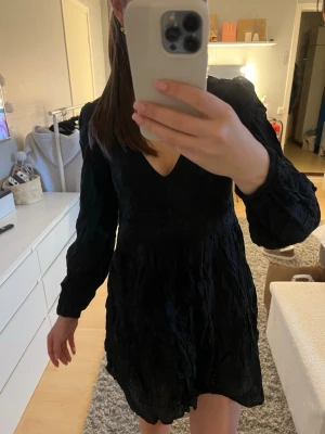 Svart kort klänning med v-ringning - Snygg svart kort klänning med v-ringning och långa ärmar. Klänningen har en lätt volang nedtill och markerad midja. Den är från Zara och har broderier. Storlek XS. Skriv om du undrar nått💕