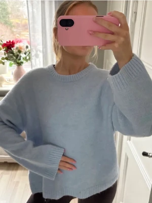 Ljusblå stickad tröja - Helt oanvänd ljusblå stickad tröja med rund halsringning. Tröjan har långa ärmar och breda ribbade muddar vid ärmslut och nederkant. Stolek S.