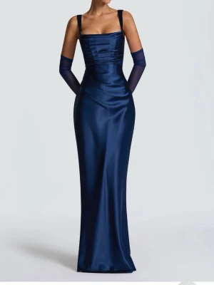 Marinblå långklänning i satin - Elegant marinblå långklänning i glansigt satinmaterial med smala axelband och figurnära passform. Klänningen har snörning i ryggen vilket gör att den passar både S och M & kan justeras utifrån önskad passform. Perfekt för dig som vill sticka ut på bal eller fest