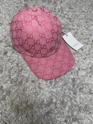 Rosa Gucci keps med GG-mönster helt riktigt och helt nytt - Snygg rosa keps från Gucci med det klassiska GG-monogrammet över hela kepsen. Kepsen har böjd skärm och justerbar rem bak. Tillverkad i ett slitstarkt tyg som ger en exklusiv känsla. Perfekt accessoar för dig som vill sticka ut och visa stil.