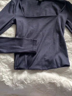 Mörkblå långärmad topp Gina Tricot - Snygg mörkblå långärmad topp från Gina Tricot med fyrkantig ringning. Tillverkad i mjuk och stretchig polyester som sitter skönt på kroppen. Perfekt att styla med jeans eller kjol för en trendig look.