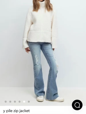 Krämvit teddyjacka med dragkedja - Mysig krämvit teddyjacka med hög krage och hel dragkedja framtill. Jackan har en avslappnad passform och är tillverkad i fluffigt pilematerial som ger en soft look. Perfekt för lager på lager och enkel att matcha med jeans eller kjol.