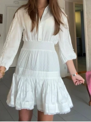 Vit skjortklänning från Maje - Supersöt vit skjortklänning från Maje med knappar framtill, markerad midja och volangkjol. Klänningen har trekvartsärmar med dekorativa detaljer längs ärmarna och är gjord i ett lätt, luftigt tyg. Perfekt för sommarens alla tillfällen! Endast använd 1 gång💗