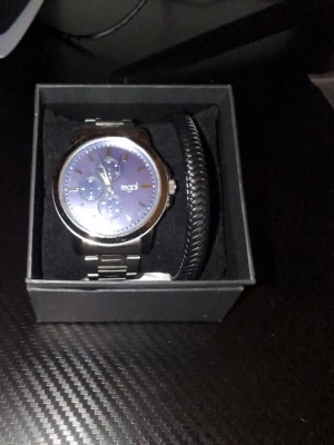 Silverfärgad klocka från Regal - Stilren klocka från Regal med silverfärgat metallarmband och blå urtavla. Klockan har tre mindre urtavlor och levereras i originalask tillsammans med ett svart flätat armband och extra länkar för justering.