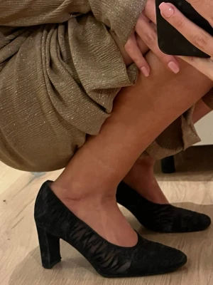 Retro Svarta pumps med mesh mönster - Säljer ett par retro svarta pumps med bred klacka  och spetsig tå. Skorna har ett transparent meshparti med zebramönster som ger en cool och trendig look. Perfekta för dig som vill sticka ut lite extra. Materialet är en mix av mockaimitation och mesh.