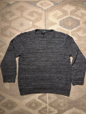 Svartmelerad stickad tröja H&M - Stickad tröja från H&M i svartmelerat garn med rund halsringning och långa ärmar. Tröjan har en avslappnad passform och ribbade muddar vid ärmslut och nederkant. Perfekt för lager på lager och enkel att matcha med jeans.