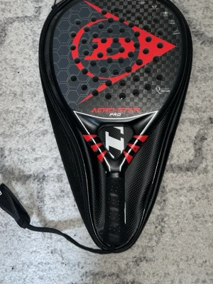 Dunlop Aero-Star Pro padelracket 2025 - Diamant format kraftfullt Padelracket med carbonfiber vilket genererar väldigt mycket kraft och är väldigt bra generellt(specifikationer på sista bild) grepp lindan har släppt lite längst ner men märks knappt av sedan är de fåtal repor på racket så den är i väldigt bra skick. Perfekt för dig som vill ta dig till nästa nivå. Läder fodral ingår. Nypris 3495 kr 