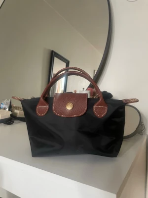 Svart Longchamp Le Pliage handväska - Klassisk svart Longchamp Le Pliage handväska i nylon med bruna läderdetaljer🤎