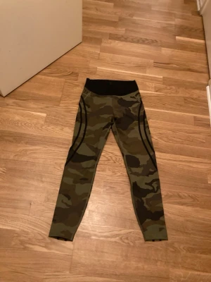 Camo träningstights från Better Bodies stl M - Snygga träningstights från Better Bodies i camomönster med svarta detaljer längs benen och bred svart midjeresår. Perfekta för gymmet eller löprundan, tillverkade i stretchigt funktionsmaterial som andas.