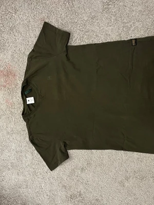 Röd och Mörkgrön t-shirt från G-Star och Tommy hilfiger - Säljer en mörkgrön t-shirt från G-Star RAW i storlek M. T-shirten har klassisk passform, rund hals och korta ärmar. Materialet är mjuk bomull och den har en diskret logga på bröstet. Perfekt för dig som gillar stilrena basics.