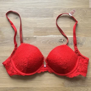 Röd spets push-up bh från Victoria's Secret - Säljer en snygg röd push-up bh från Victoria's Secret med spetsdetaljer och justerbara axelband. Bh:n har vadderade kupor
