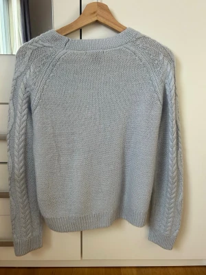 Ljusblå kabelstickad tröja H&M - Snygg ljusblå kabelstickad tröja från H&M med rund halsringning och ribbade muddar. Tröjan har ett klassiskt flätmönster framtill och på ärmarna, vilket ger en trendig och mysig look. Perfekt att matcha med jeans eller kjol.